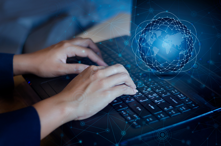 Hands typing on a laptop keyboard, with a glowing blue globe and network overlay on the screen.