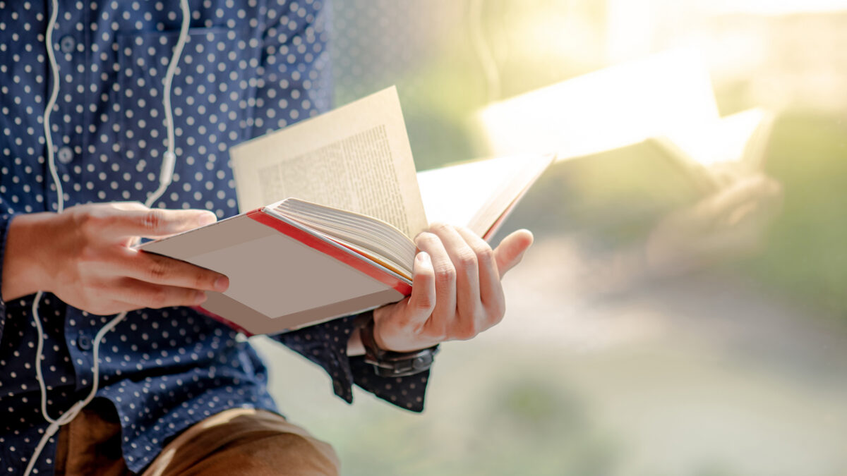 Close-up of a person in a polka-dot shirt and headphones reading a book outdoors in sunlight