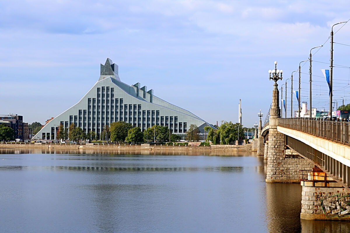 The National Library of Latvia, a modern, angular building, across a river from a stone bridge.