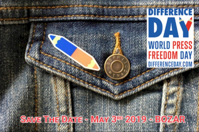 A denim jacket with a pencil-shaped pin and a round button, next to a white banner for Difference Day.