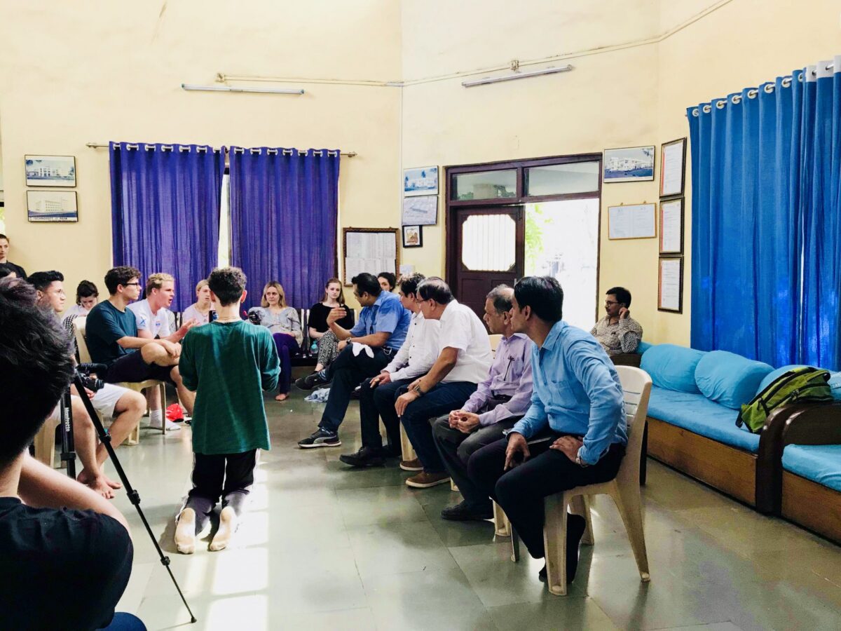 A group of young people and adults sitting in a room, with one young person kneeling in the foreground.