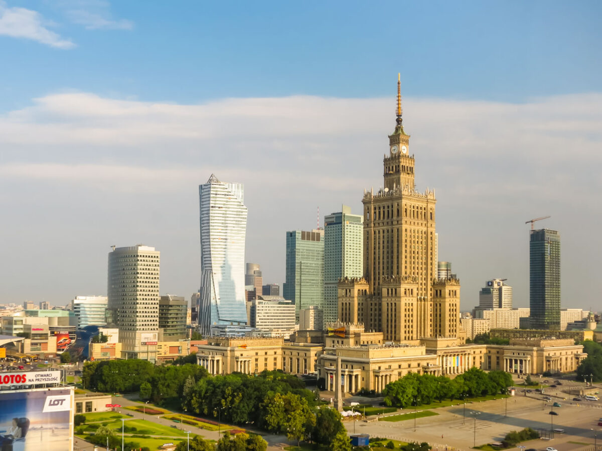 Warsaw skyline with the Palace of Culture and Science and modern skyscrapers under a blue sky.