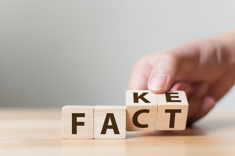 A hand placing a wooden block with 'KE' on top of 'CT', changing 'FACT' to 'FAKE'.