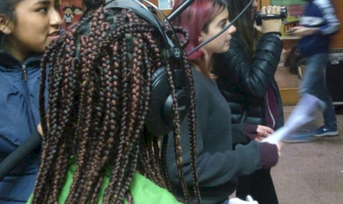 Three young people, one with headphones, another holding a video camera, in an indoor setting.