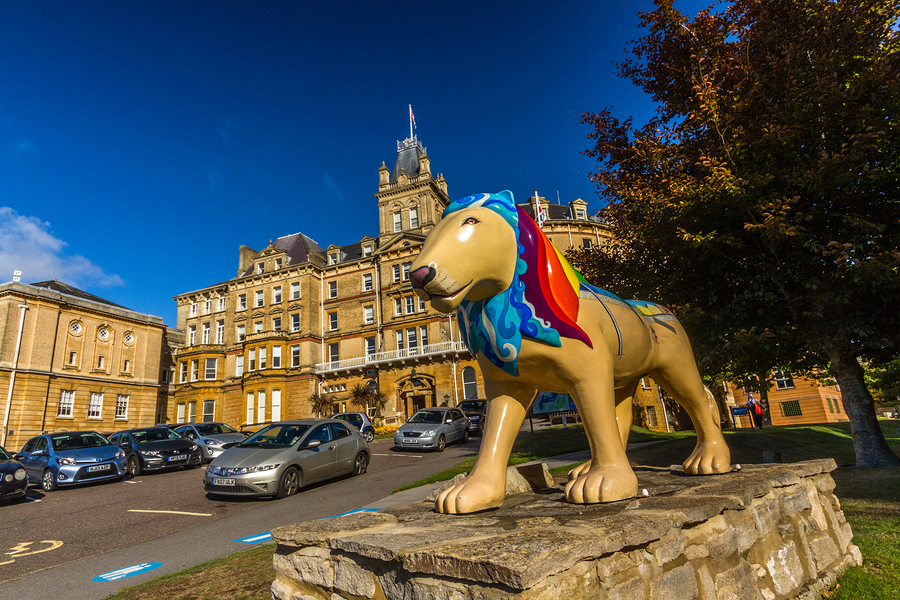 A colourful lion statue in front of a large, ornate building with cars parked on a road.