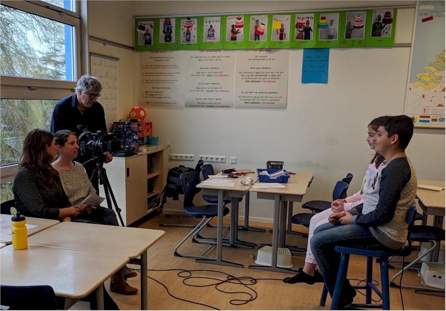 Two women and a man filming two children sitting at desks in a classroom.
