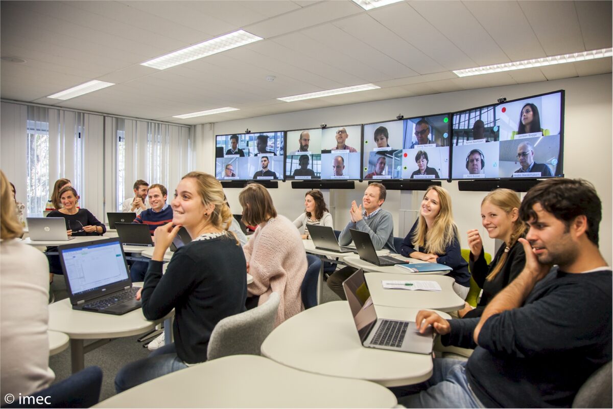 Students in a hybrid classroom with a large video wall showing remote participants