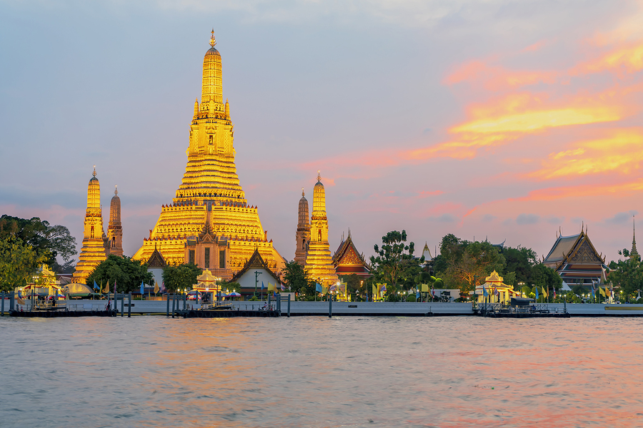 Wat Arun Temple in Bangkok, Thailand, illuminated at sunset, viewed across the Chao Phraya River.