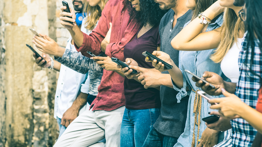A group of young people standing in a line, all looking down at and interacting with their smartphones.