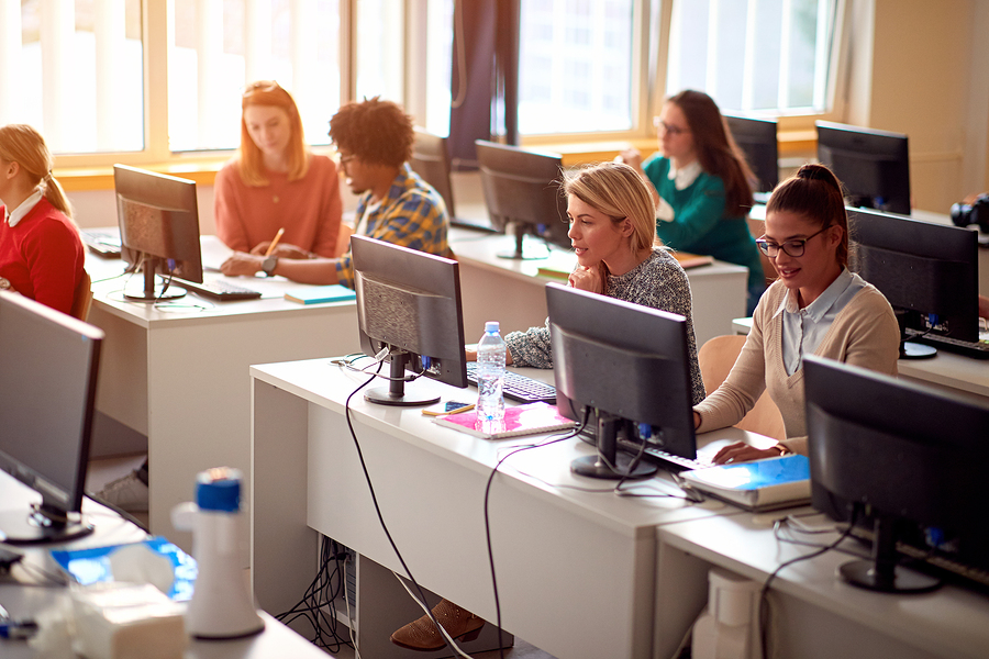 Students in a computer lab, working at individual desks with desktop computers.