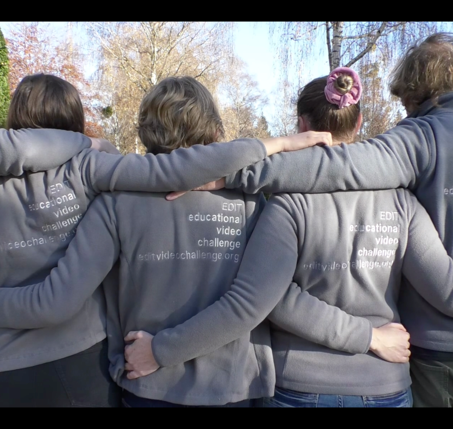 Four people seen from behind, wearing grey sweatshirts with "EDIT educational video challenge" printed on them.