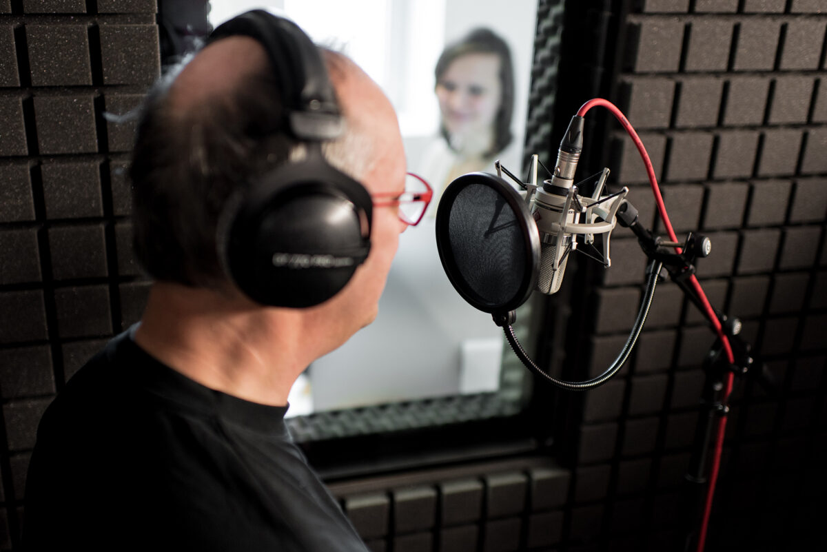 Man with headphones and red glasses recording into a microphone in a soundproofed studio