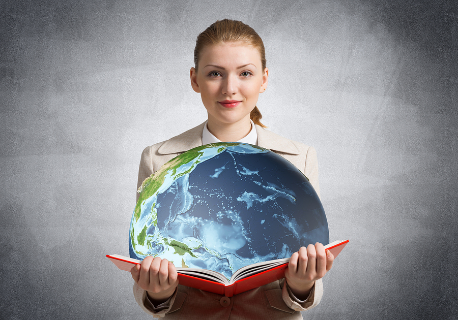 Woman in a beige jacket holding an open red book with a globe of the Earth emerging from it