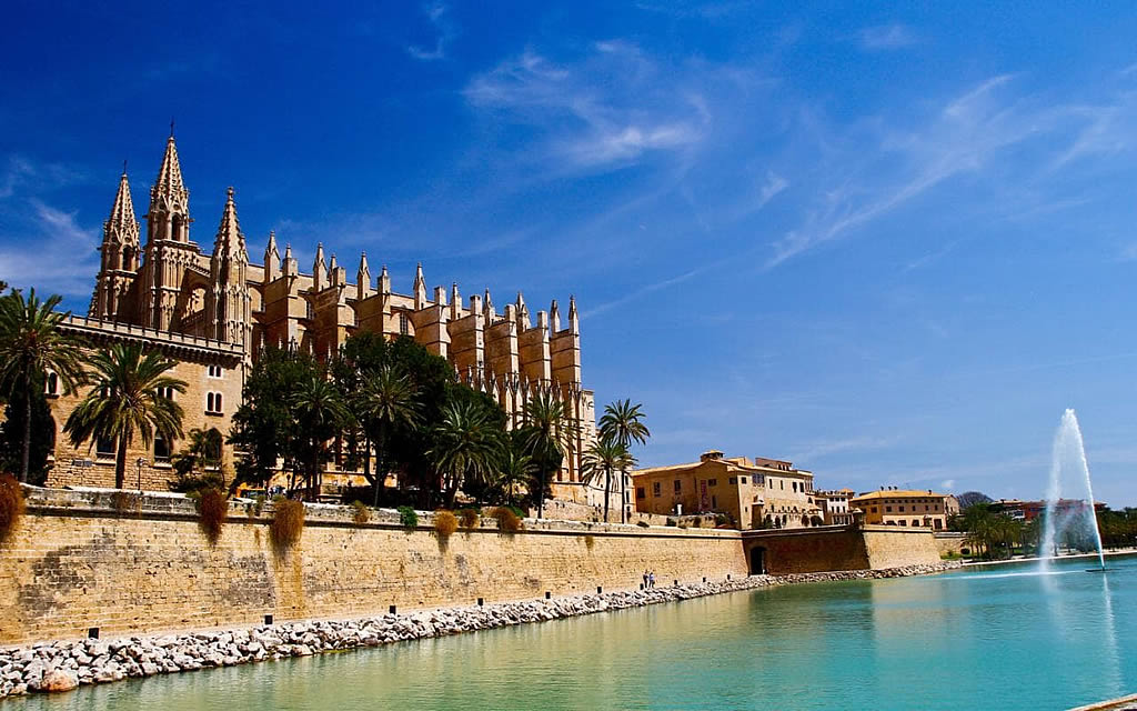 Palma Cathedral, a large Gothic building with spires, next to a body of water with a fountain