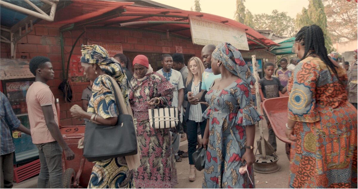 A busy street scene with several people, mostly women in colourful patterned dresses and head wraps.