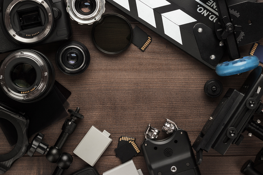 A flat lay of various video production equipment including cameras, lenses, a clapperboard, and a recorder.