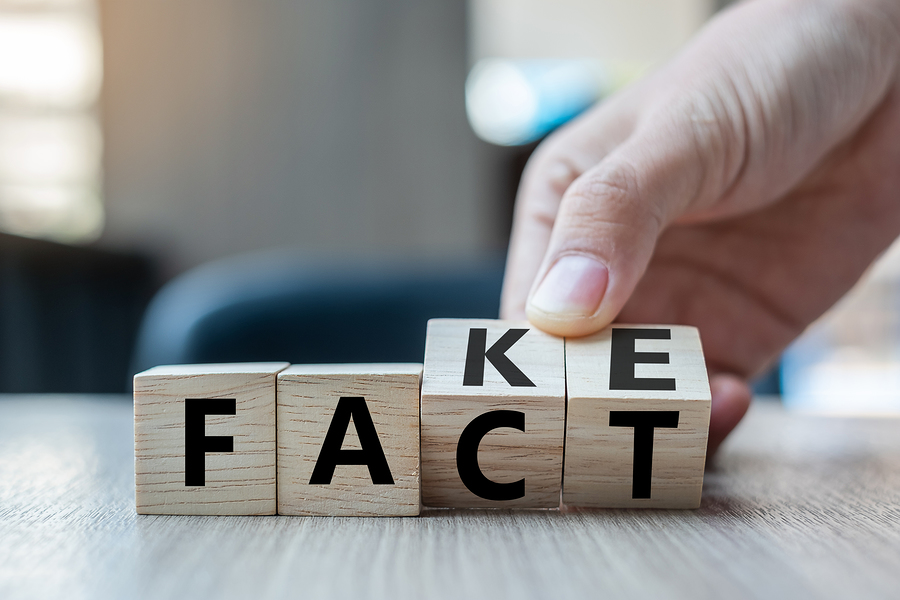 A hand placing a wooden block with the letter 'K' to change the word 'FACT' into 'FAKE'.