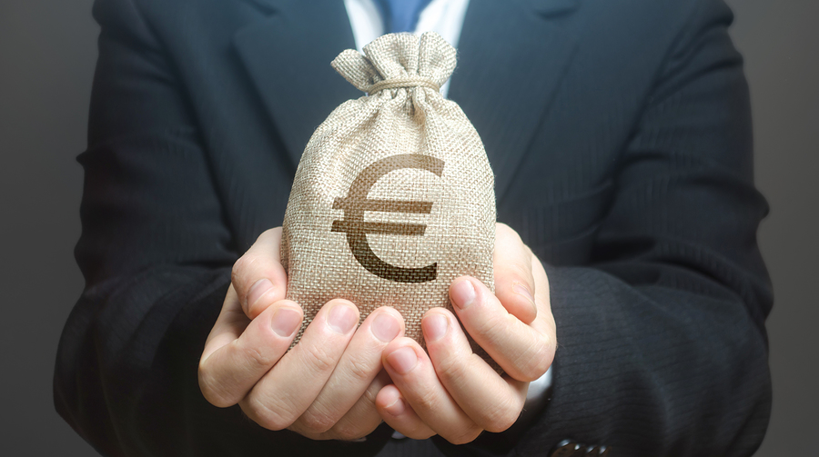 A man in a suit holds out a small hessian sack with a euro symbol printed on it.