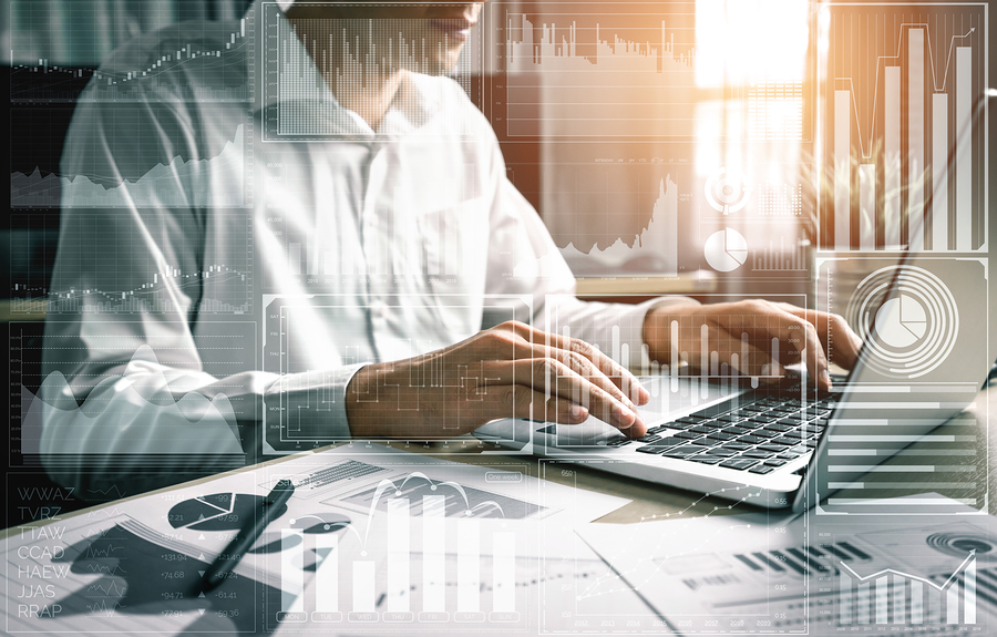 A person in a white shirt typing on a laptop, with various digital graphs and charts overlaid.