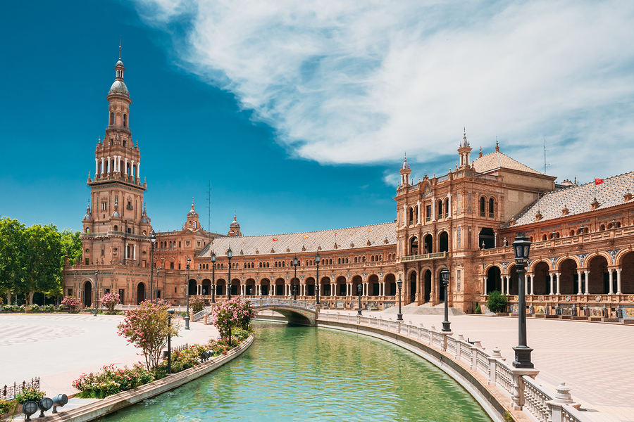 A canal with a bridge in front of a large, ornate building with a tall tower under a blue sky.