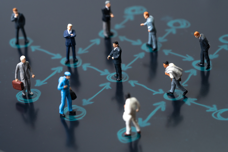 Miniature figures of people standing on a dark surface with blue arrows and circles connecting them.