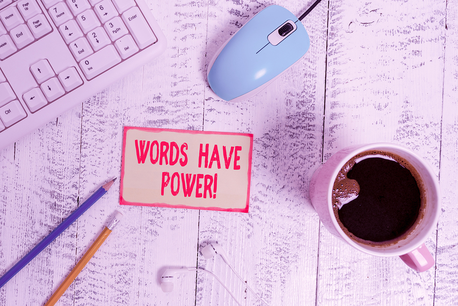 Overhead view of a keyboard, mouse, coffee mug, pencils, earphones, and a note saying Words Have Power!