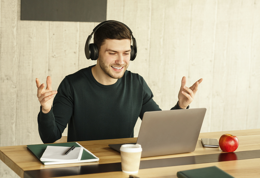 Smiling man with headphones on a video call on his laptop, gesturing with his hands.