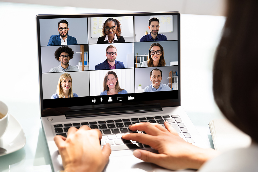 A person typing on a laptop, participating in a video conference with eight other people on screen