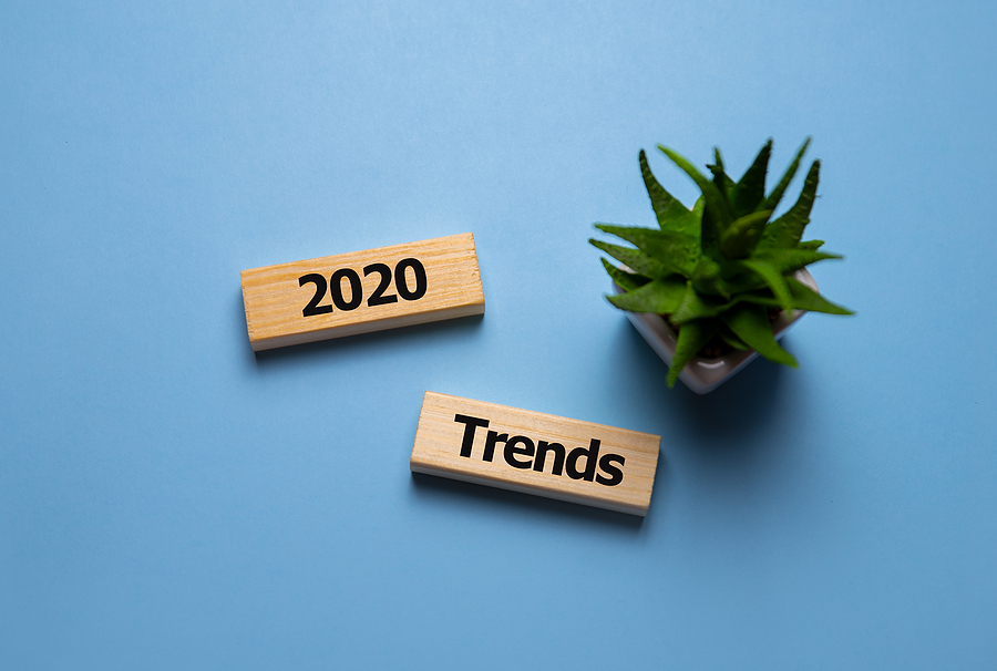 Two wooden blocks on a blue background, one says '2020' and the other 'Trends'. A small plant is next to them.