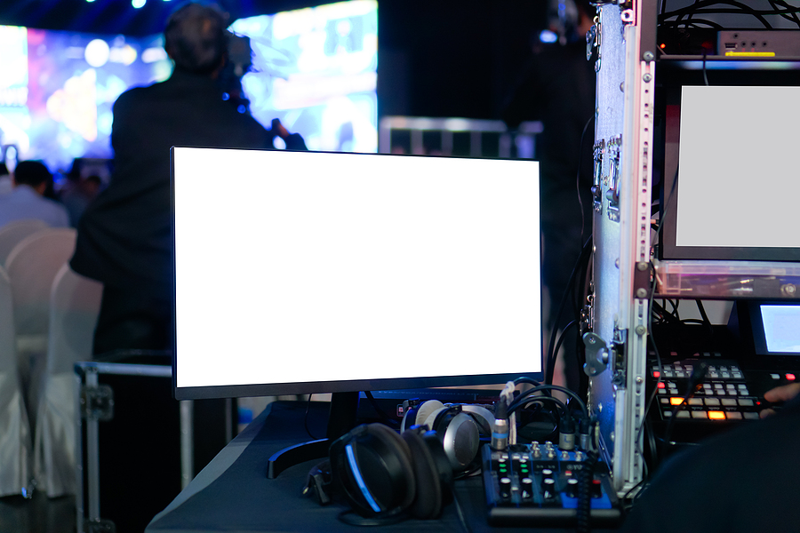 A monitor with a blank white screen, headphones, and audio equipment at a conference or event
