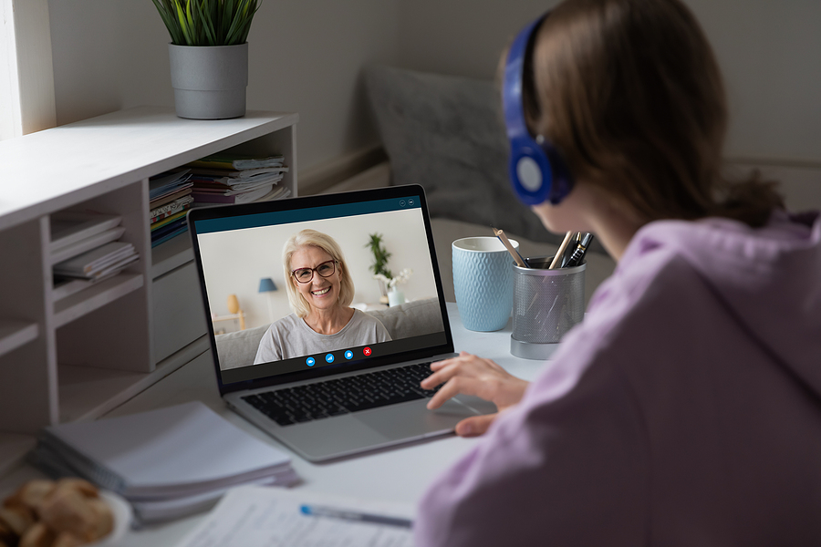 A student in headphones on a video call with a smiling older woman on a laptop.