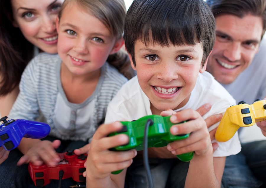 A family of four, two adults and two children, smiling and playing video games together.