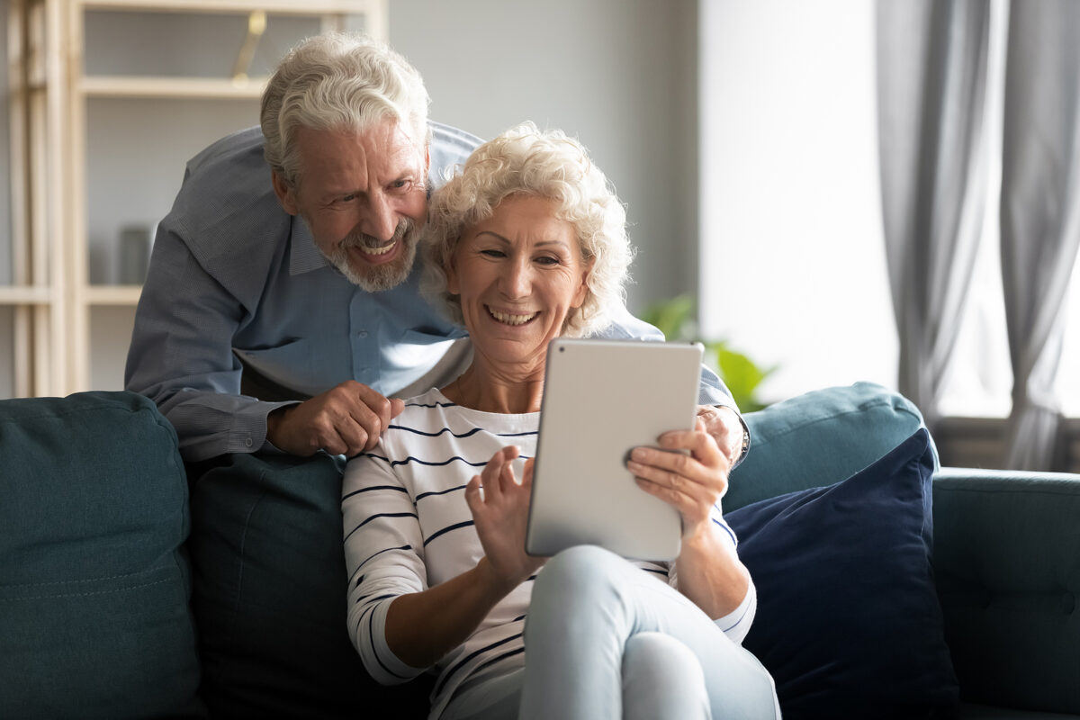 Happy older couple using a tablet computer together on a sofa, smiling and looking at the screen.