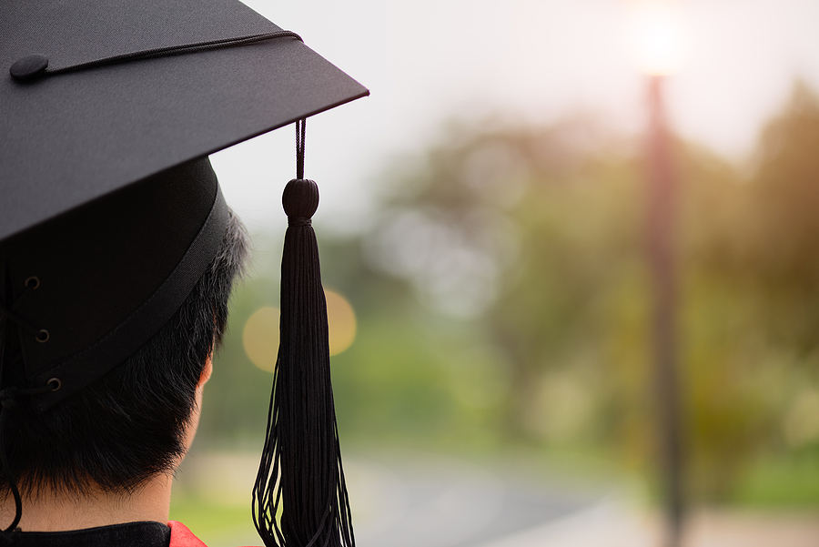 Rear view of a graduate wearing a black cap and gown, looking towards a bright light