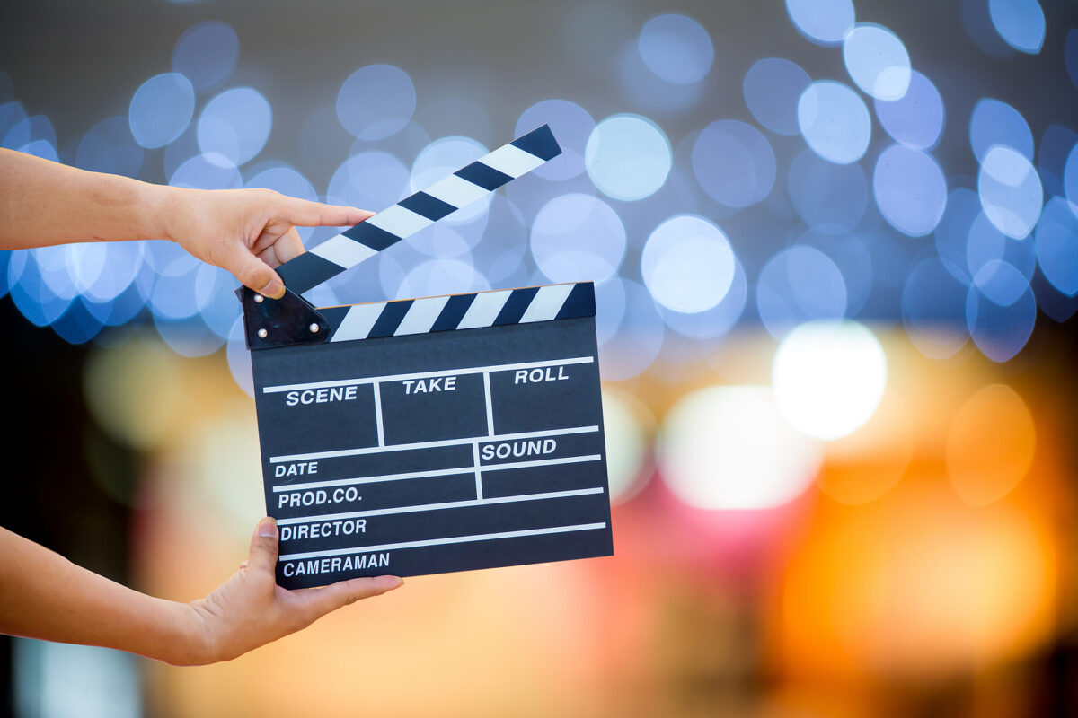 Hands holding a film clapperboard against a blurred background of blue and orange lights.
