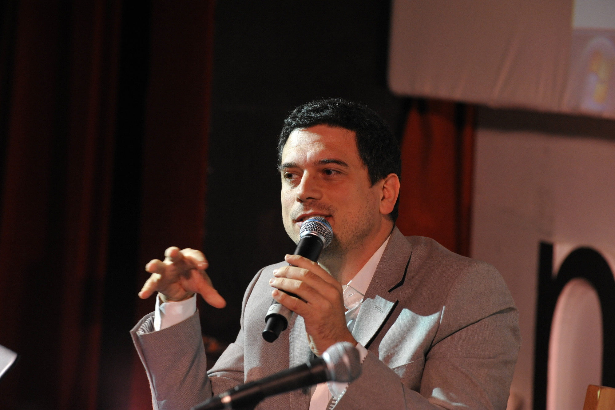 Simone Moraldi speaking into a microphone, gesturing with his left hand, at a conference