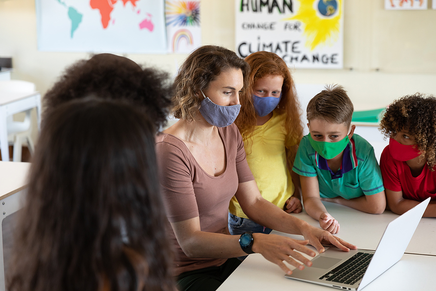 Teacher and four primary school children, all wearing face masks, looking at a laptop screen.