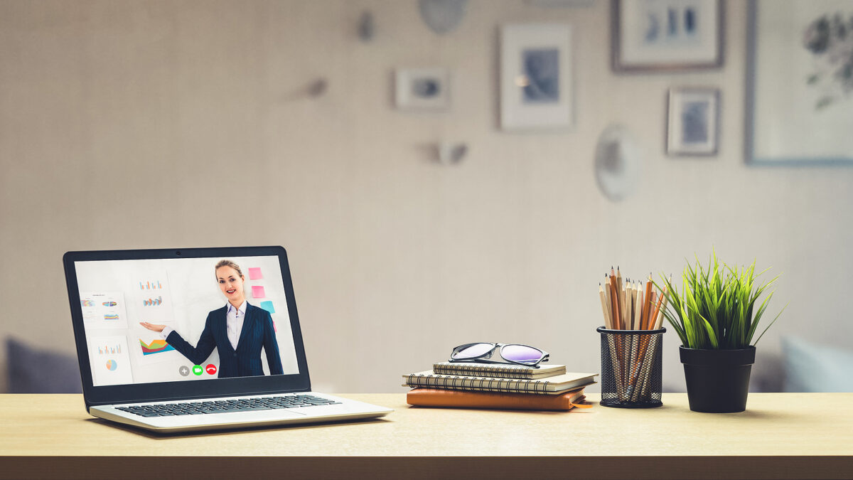 Laptop on a desk showing a woman presenting a virtual lesson with charts and graphs