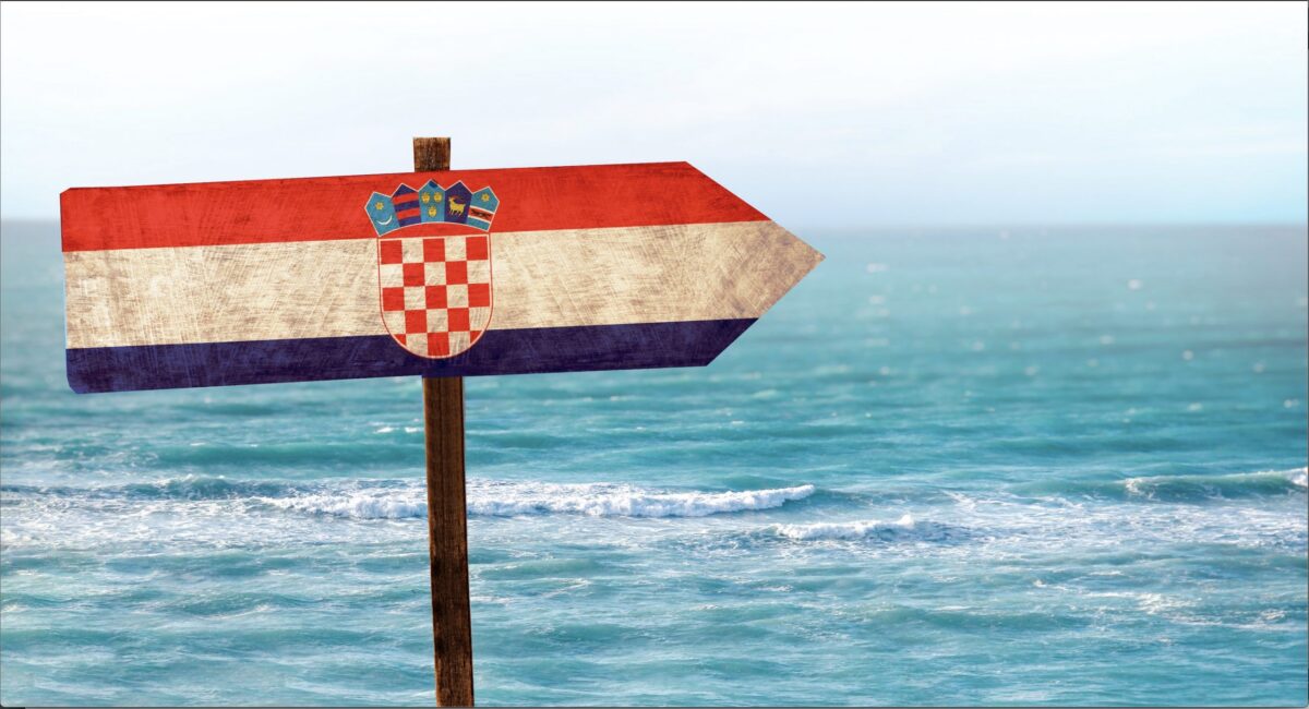 A wooden signpost with the Croatian flag pointing right towards the sea and horizon.