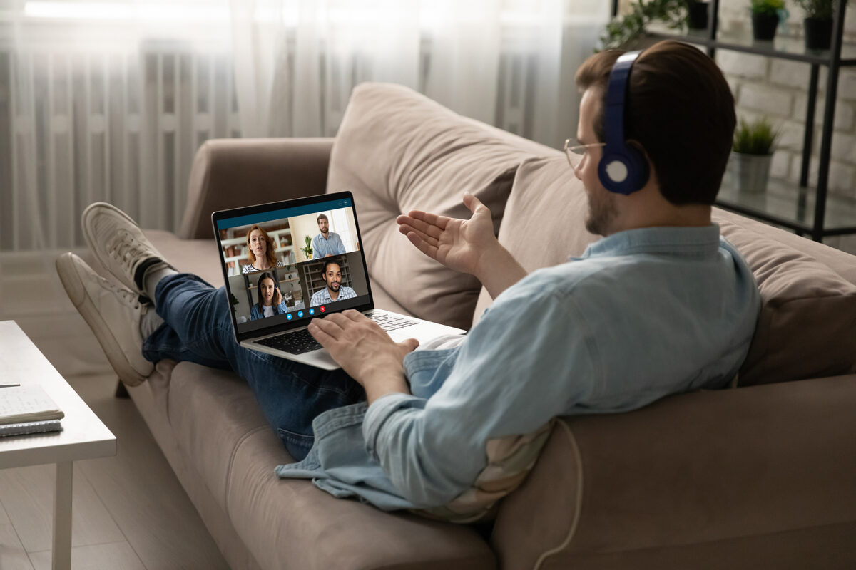 Man on a sofa, wearing headphones, on a video call with four people on his laptop.