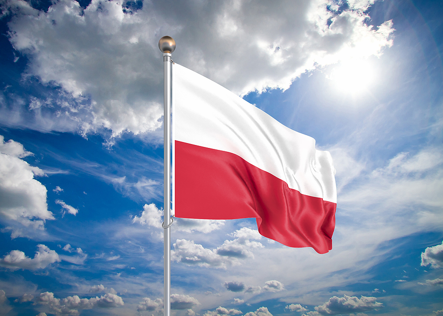 Polish flag, white over red, waving on a flagpole against a blue sky with white clouds and sun