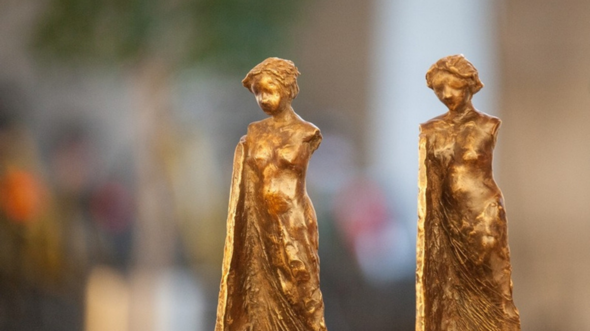 Two golden statuettes of women with draped clothing, one in focus on the left, the other blurred