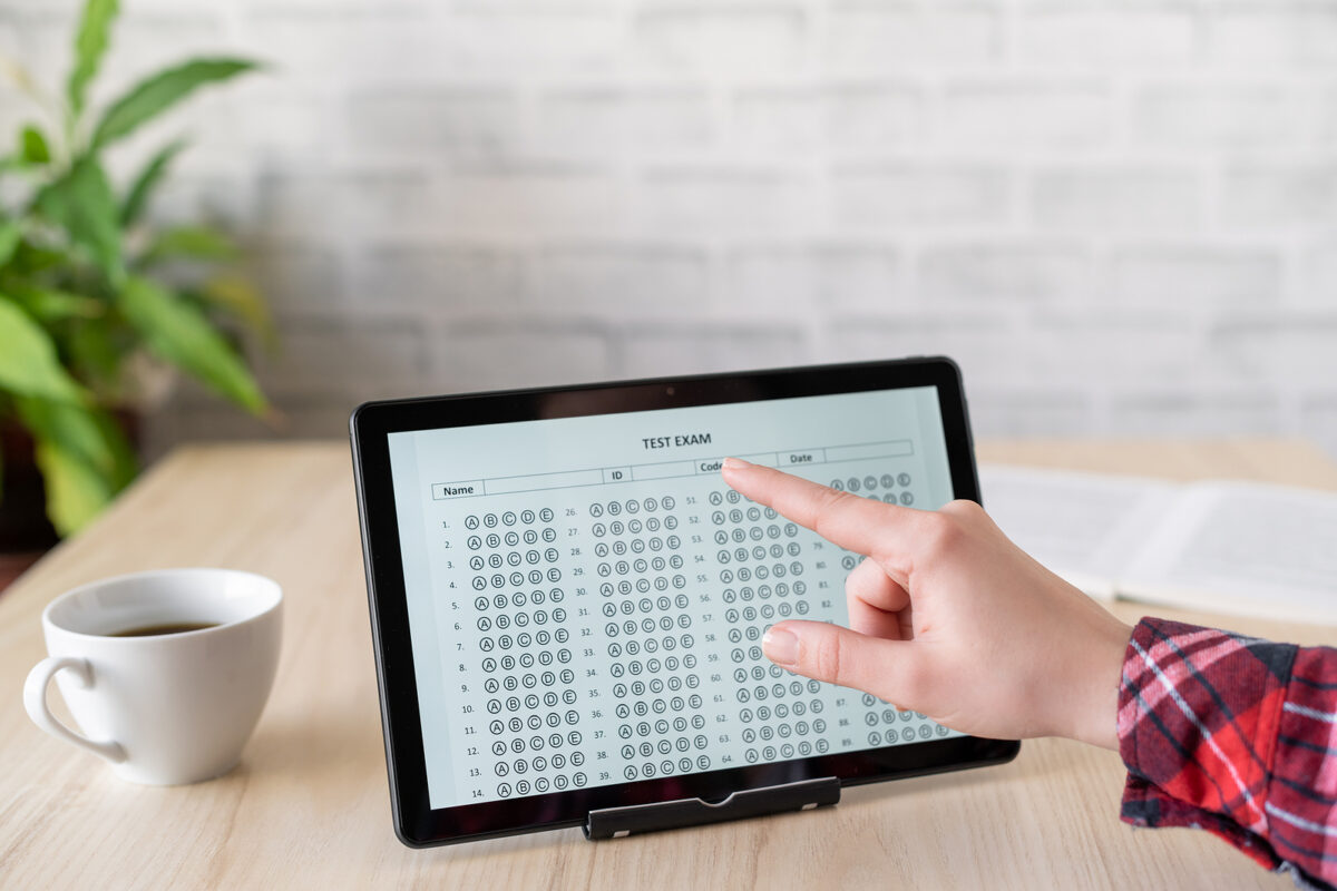 A person's hand points to a multiple-choice test form displayed on a tablet computer.