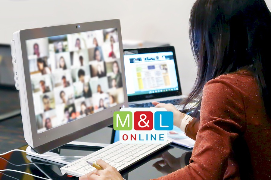 A person working on a laptop and a desktop computer showing a video conference with many participants. The Media & Learning