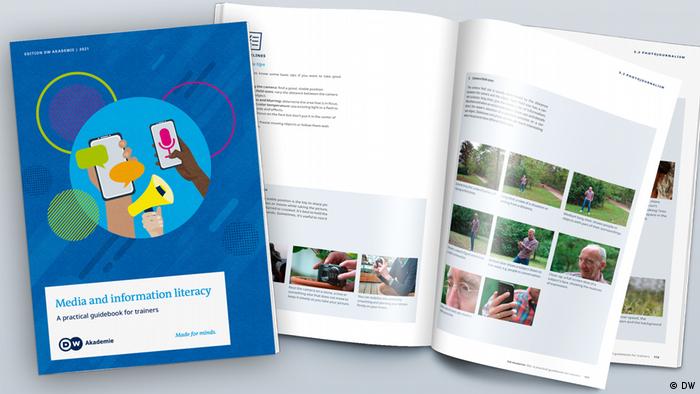 A blue book titled Media and information literacy: A practical guidebook for trainers, open to show pages with photos.