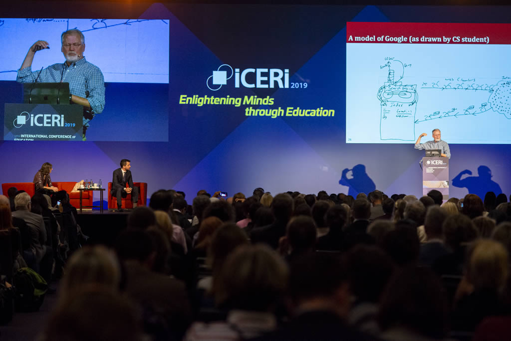 A speaker presenting on stage at the ICERI 2019 conference, with a large audience in front.