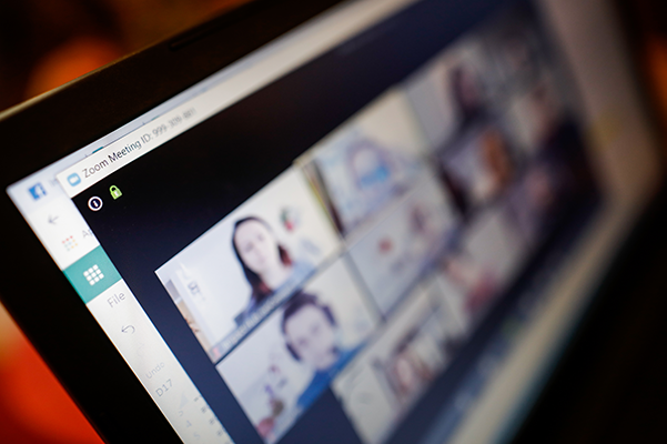 A laptop screen showing a Zoom meeting with multiple participants in a grid view, with the meeting ID visible.