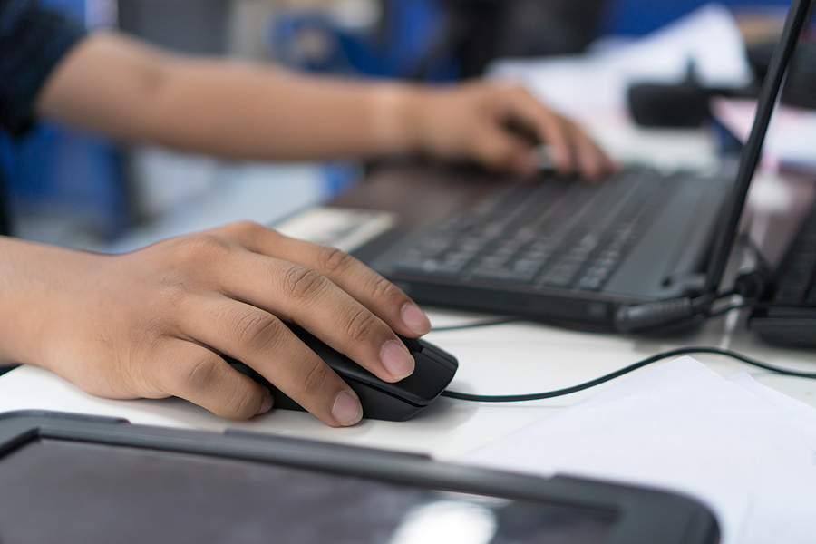 Close-up of a person's hands using a black computer mouse and typing on a laptop keyboard