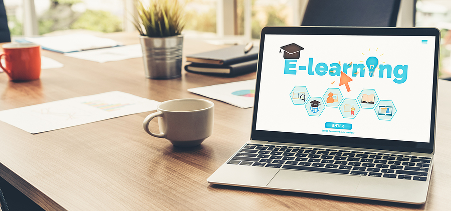 Laptop on a wooden desk displaying an e-learning website with a graduation cap and lightbulb icon
