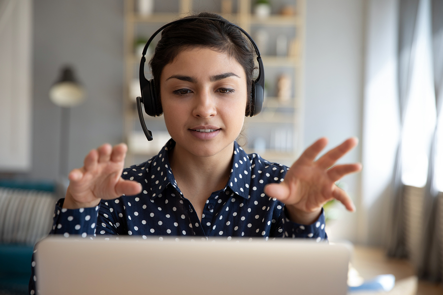 Young woman with a headset and microphone, gesturing with her hands while looking at a laptop.